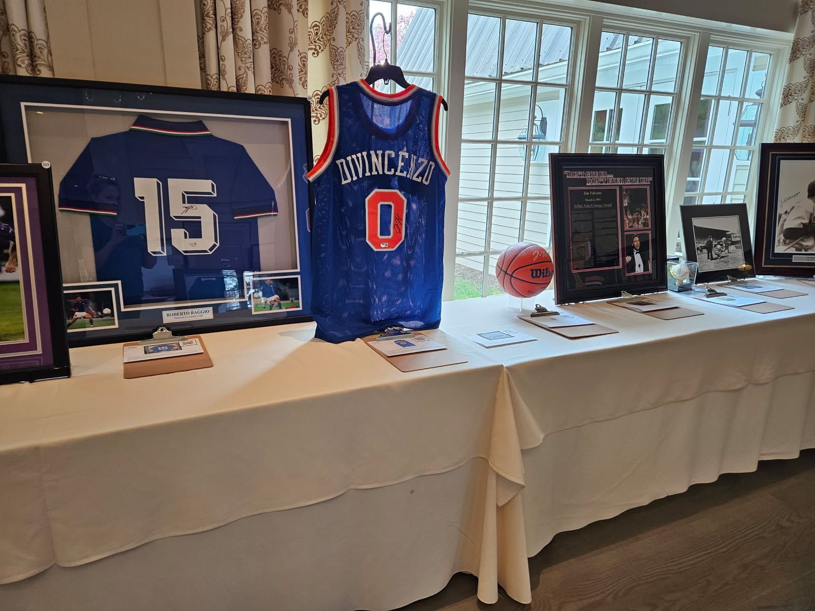A bunch of footballs , helmets , and jerseys are hanging on a wall.