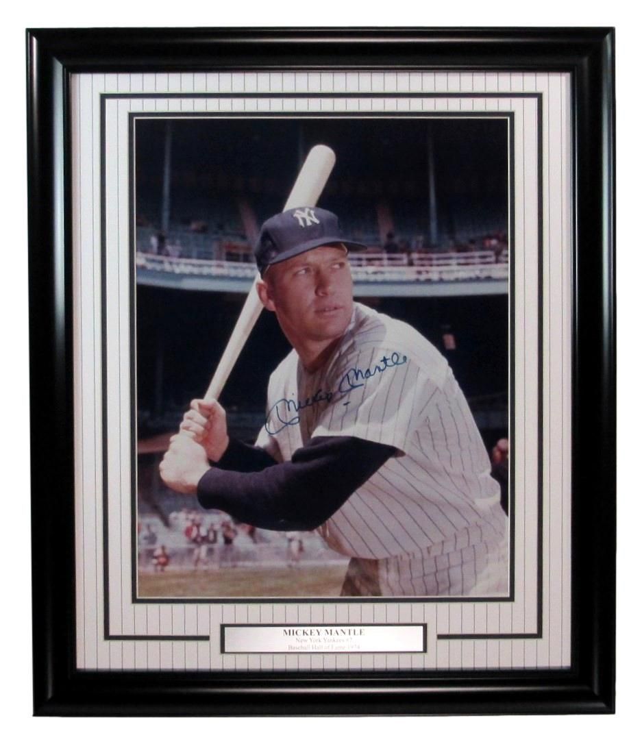Mickey Mantle in a Yankee uniform, holding a bat, in a framed photograph.