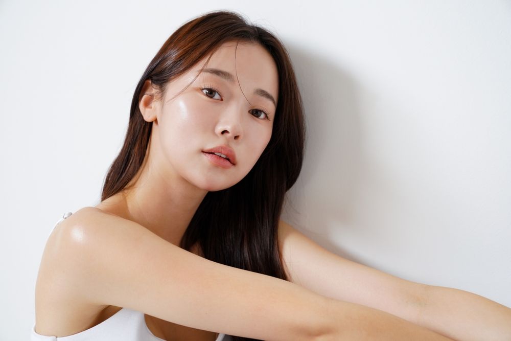 A woman with long hair is sitting in front of a white wall.