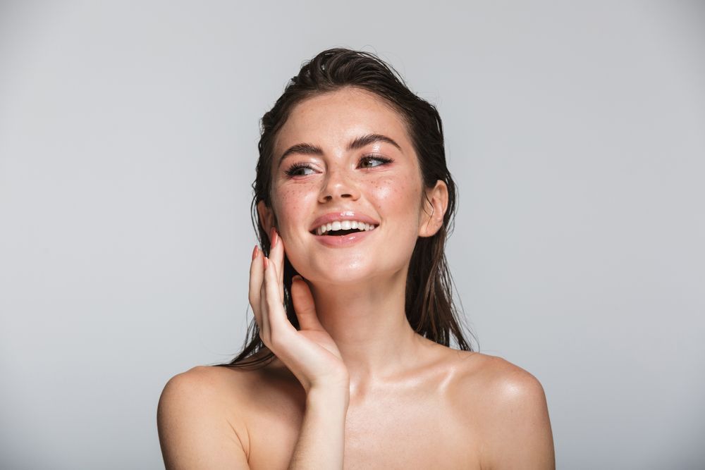Portrait of a smiling woman touching her face over gray background