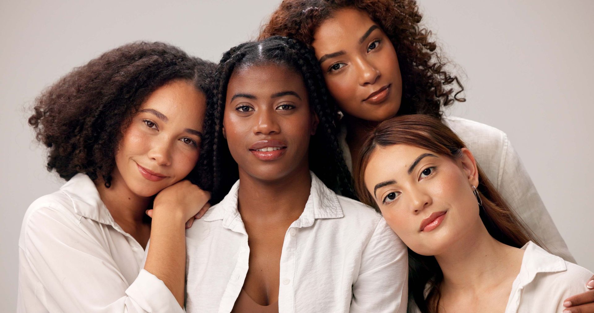 Four people in white shirts pose together against a plain light background, looking at the camera with calm expressions.