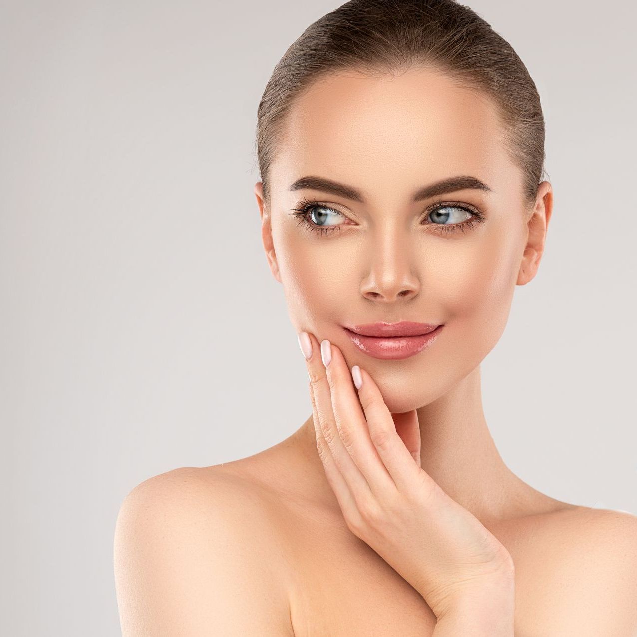 A woman is touching her face with her hand and smiling.