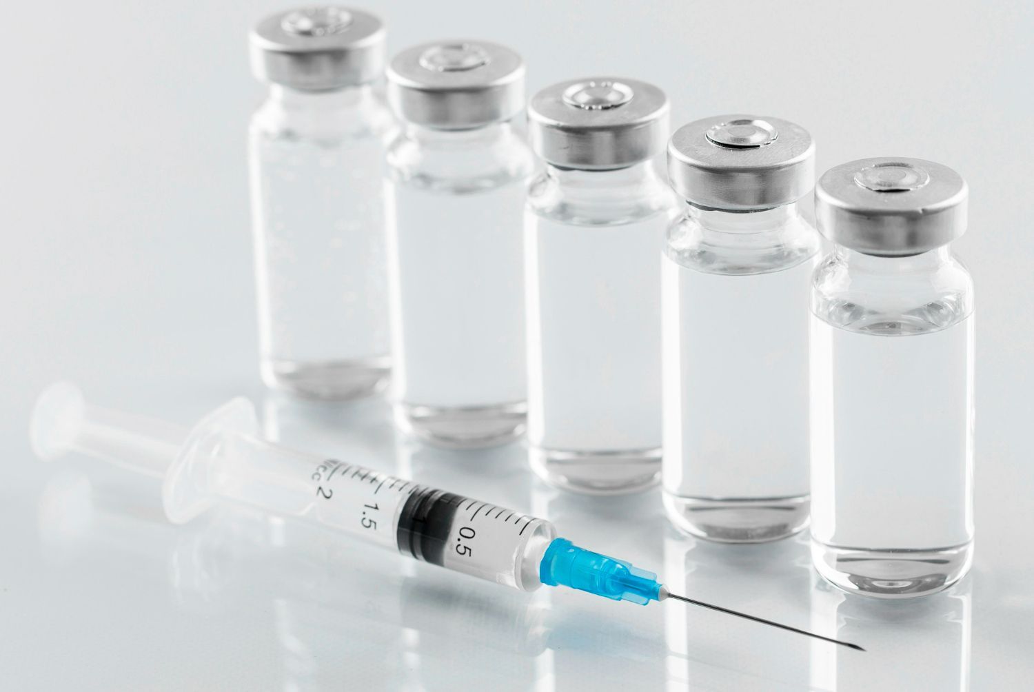 A syringe is sitting next to a row of bottles of liquid.