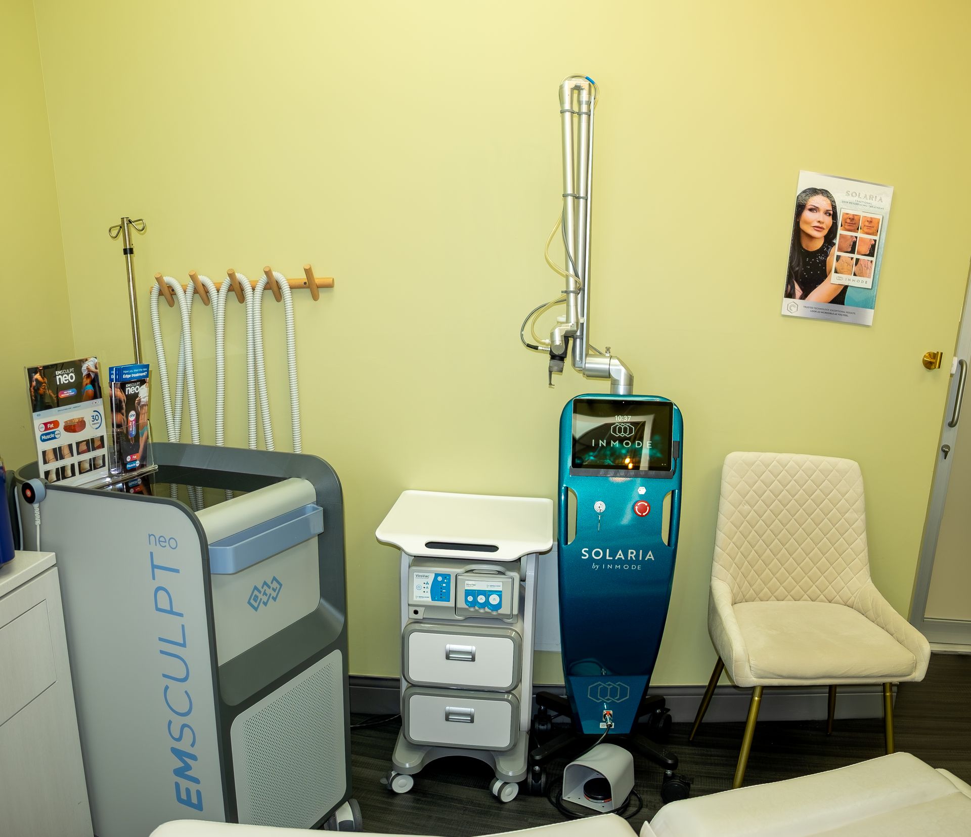 Medical office room with treatment machines, a chair, IV stands, and informational posters on the wall