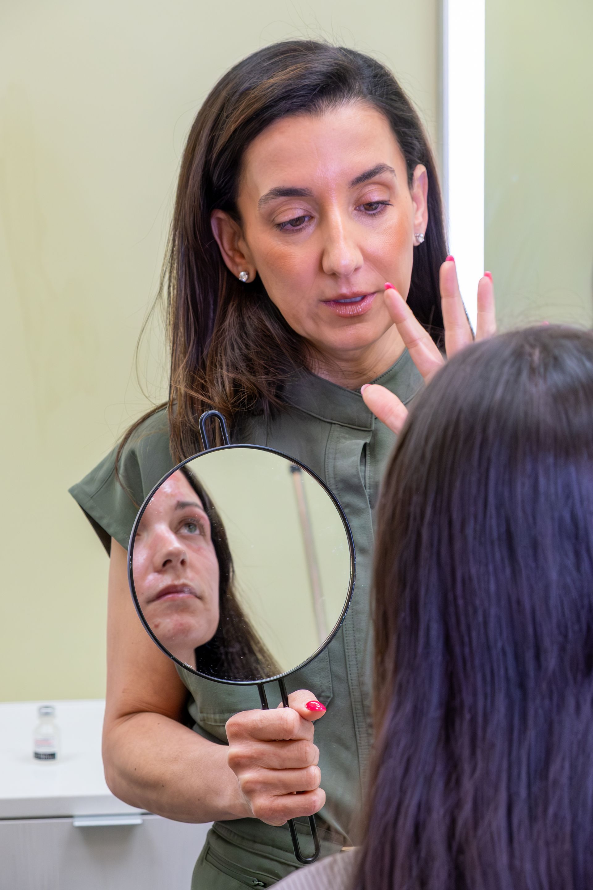 Woman demonstrating skin care with a handheld mirror, examining her face in a salon setting