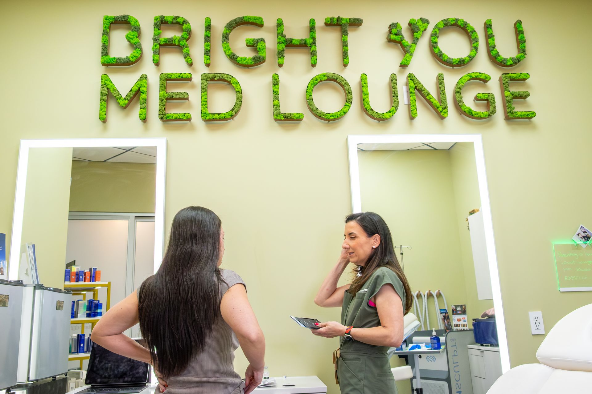Clinic reception area with green “Bright You Med Lounge” sign and two people talking at the counter