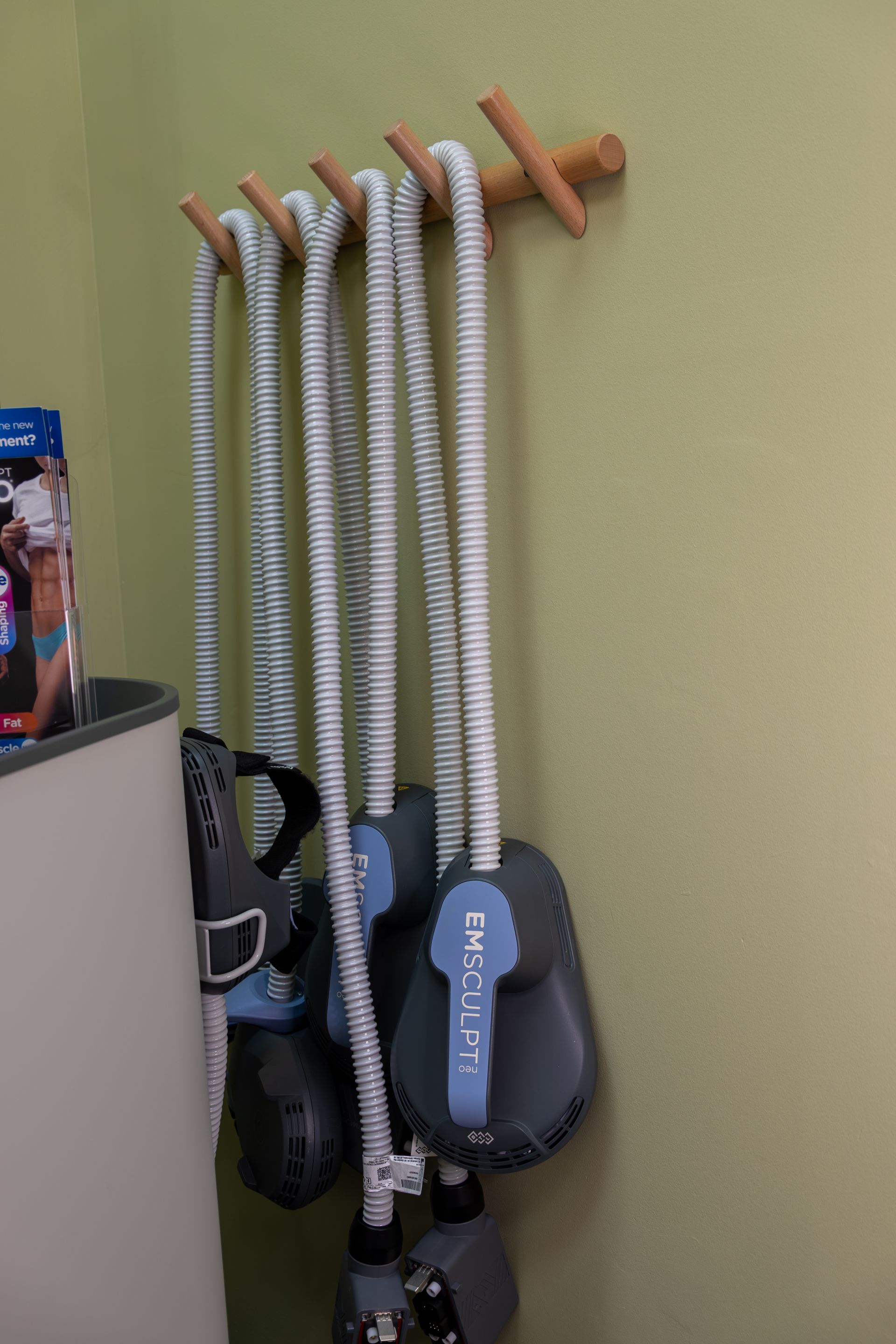 Several jump ropes and a black hand massager hanging on wall hooks against a beige wall