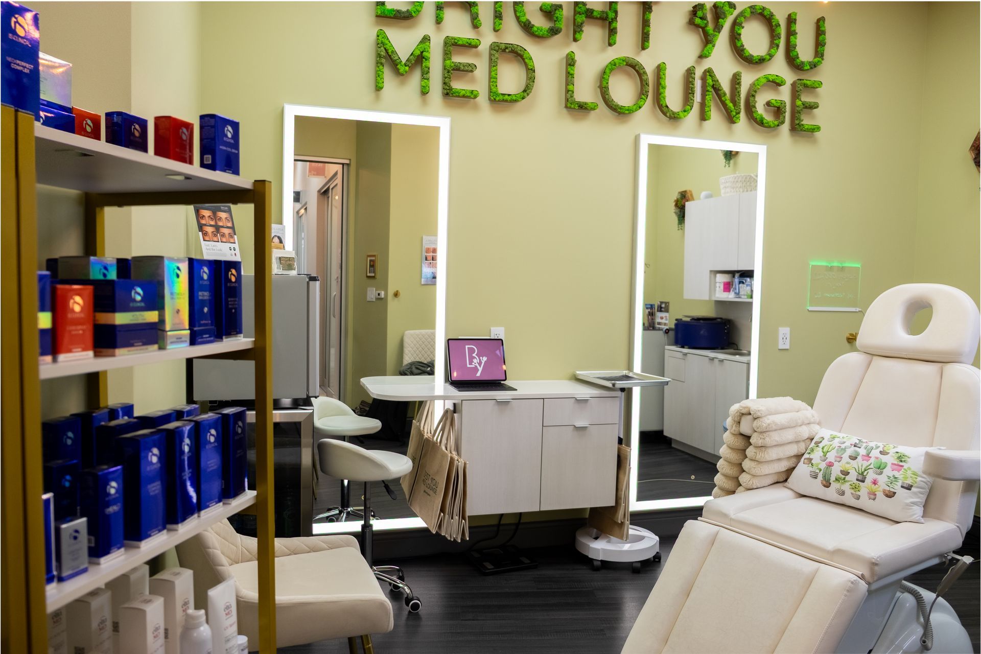 Interior of a medical spa, with a treatment chair, mirrors, shelves of products, and a work area.