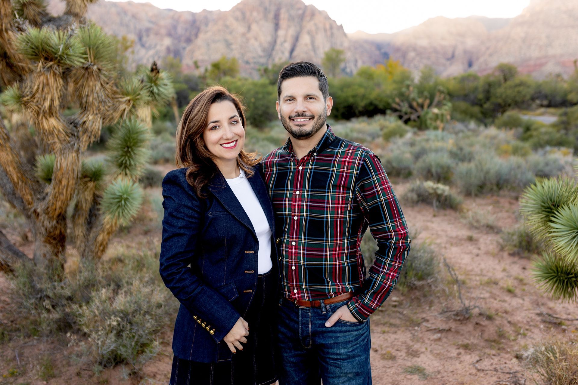 Couple posing outdoors; woman in blue blazer, man in plaid shirt, desert backdrop.