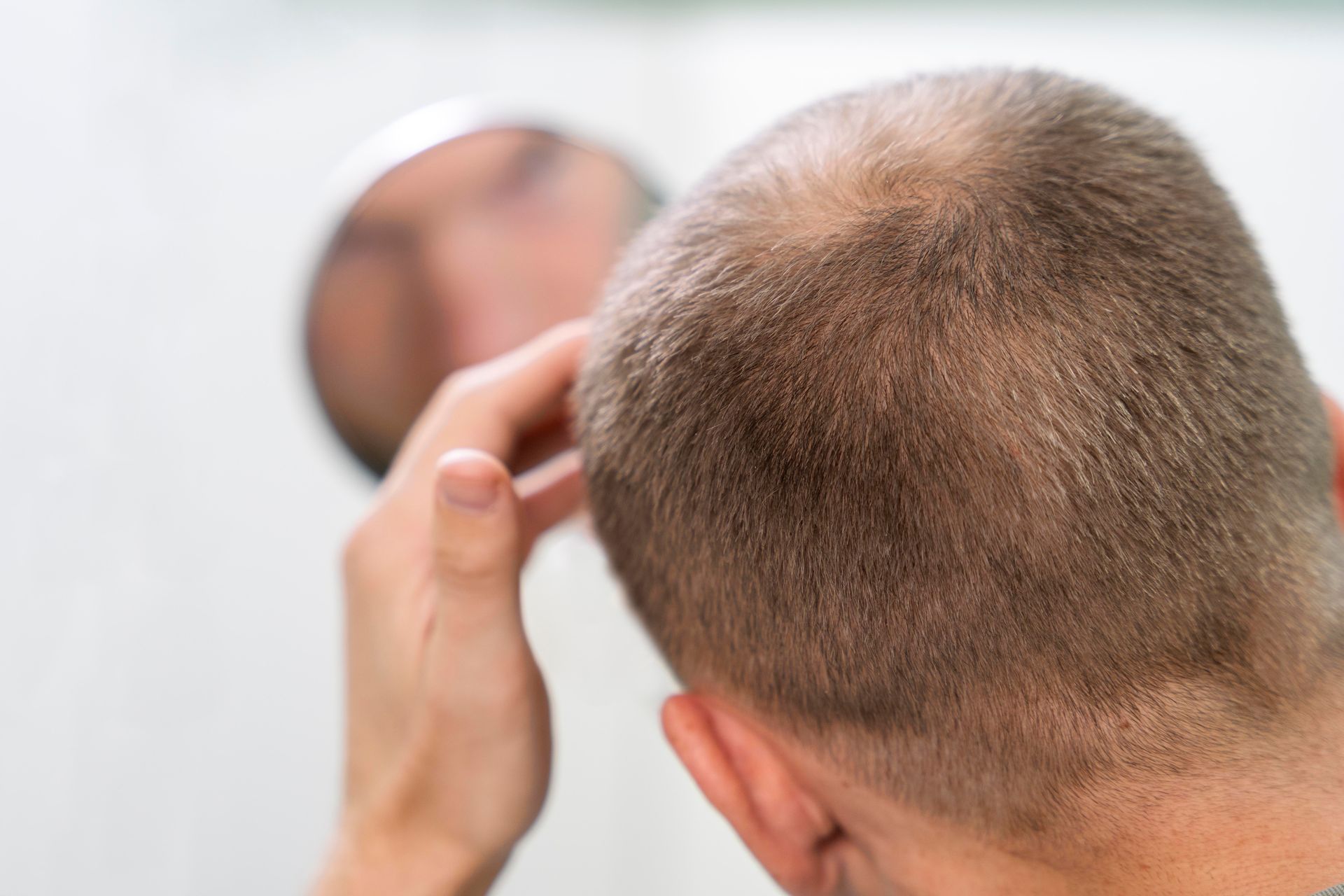 A man is looking at his hair in a mirror.