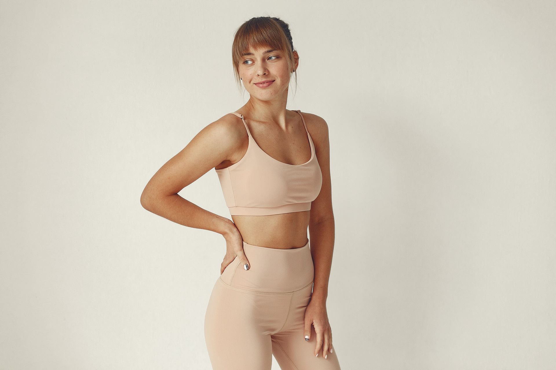 A woman in a crop top and leggings is standing with her hands on her hips.