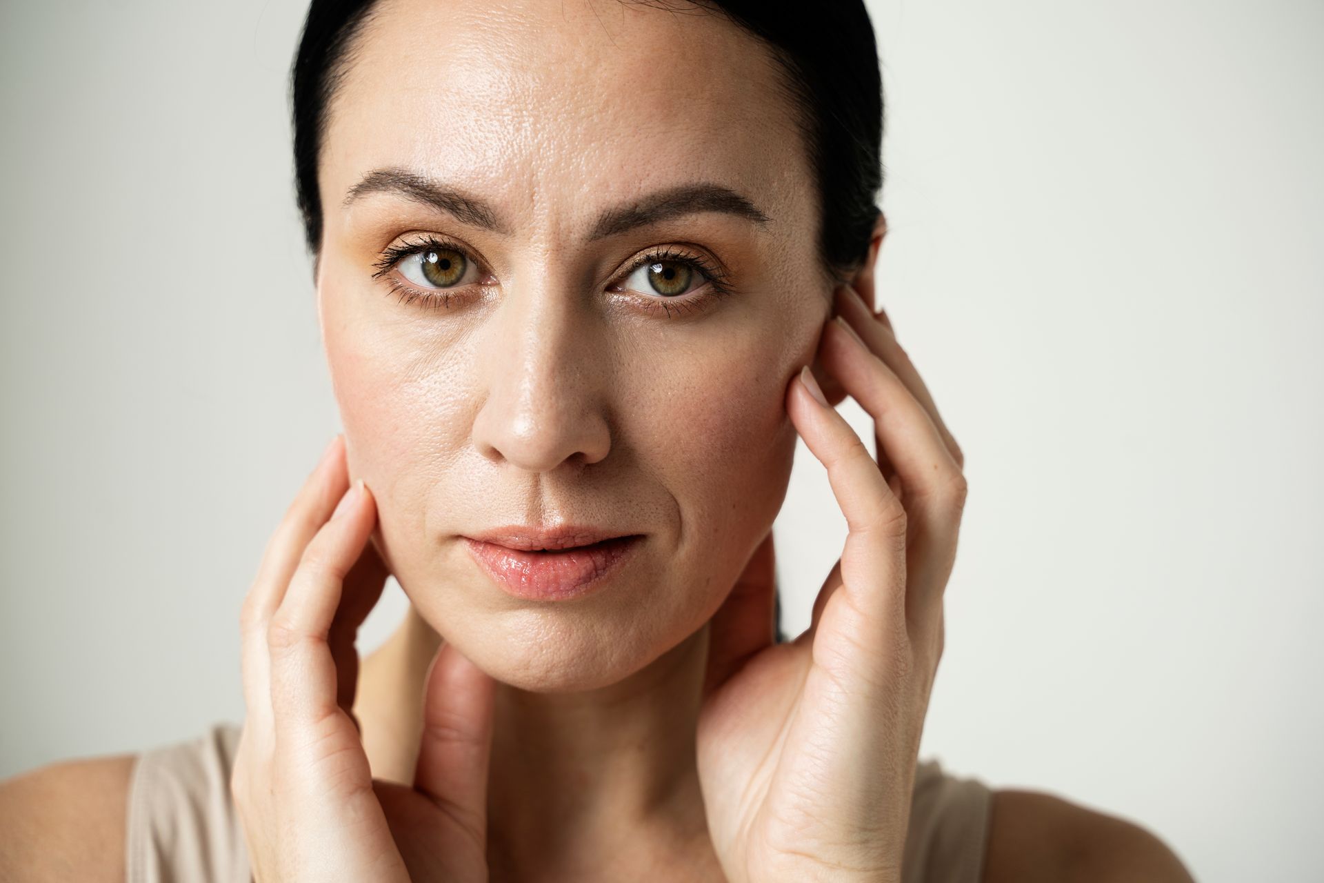 A woman is holding her face with her hands and looking at the camera.