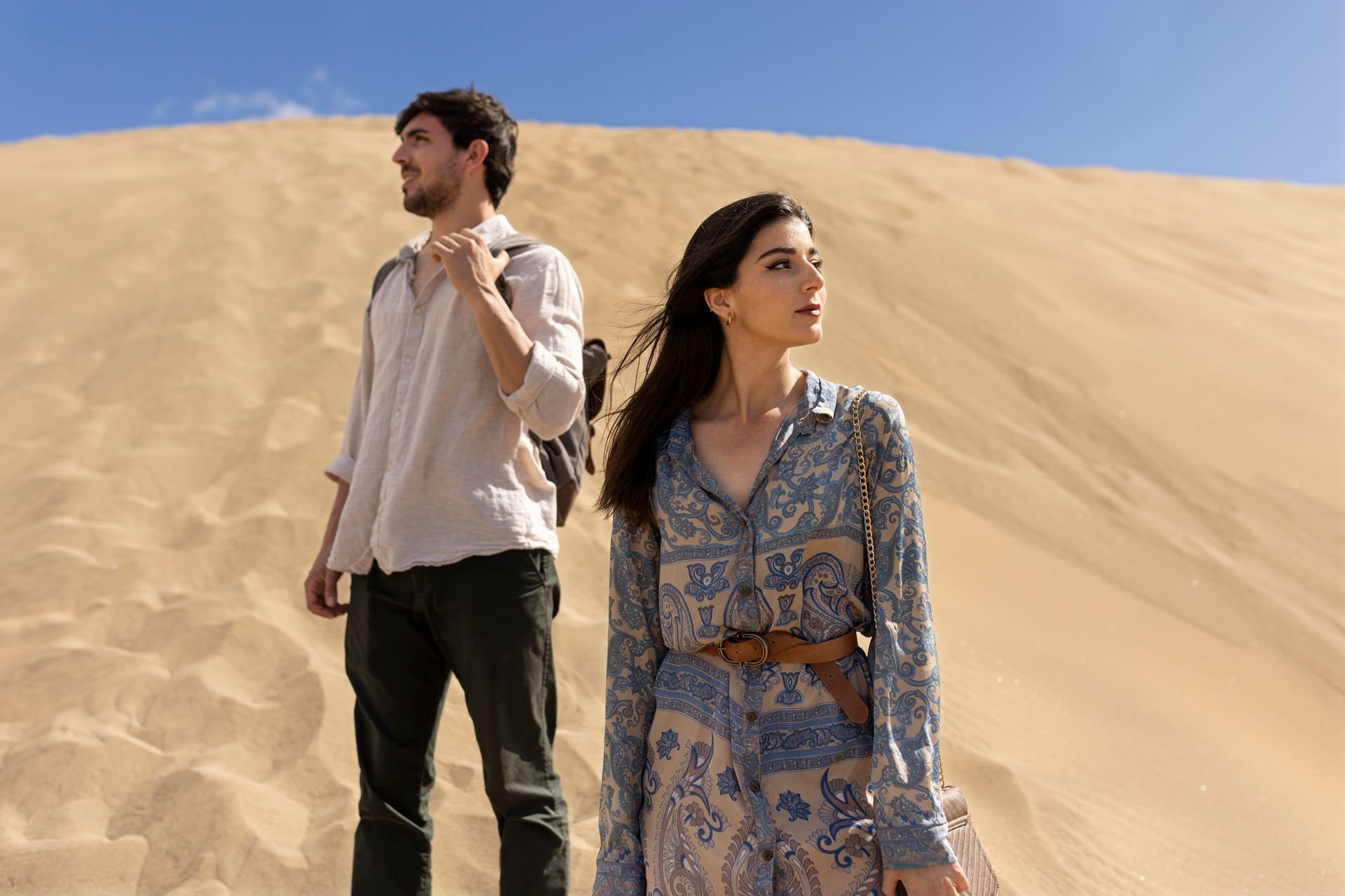 A man and a woman are standing on top of a sand dune.