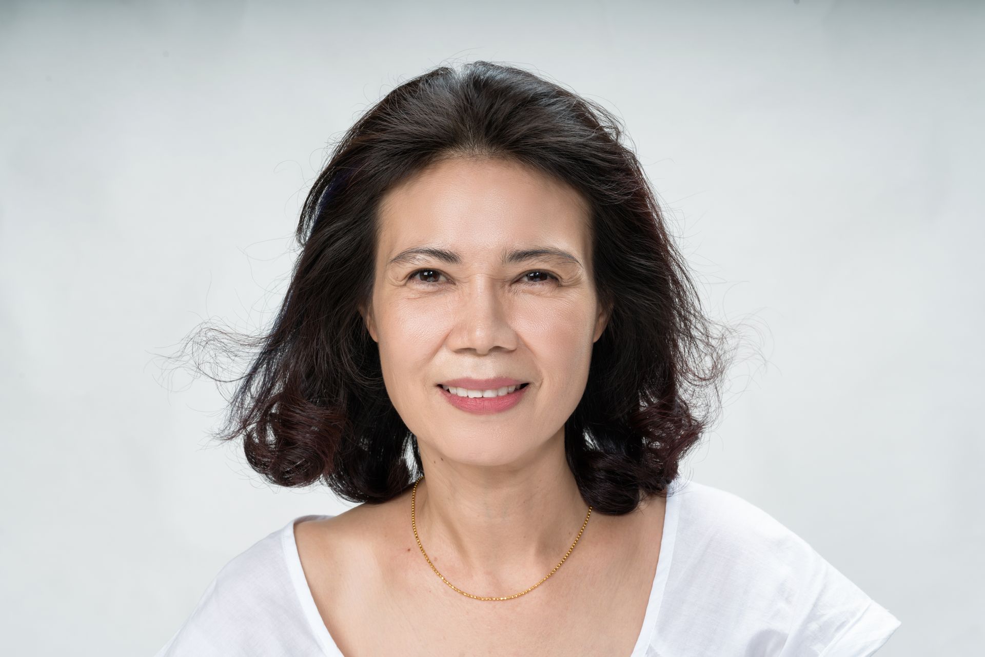 A woman wearing a white shirt and a gold necklace is smiling for the camera.