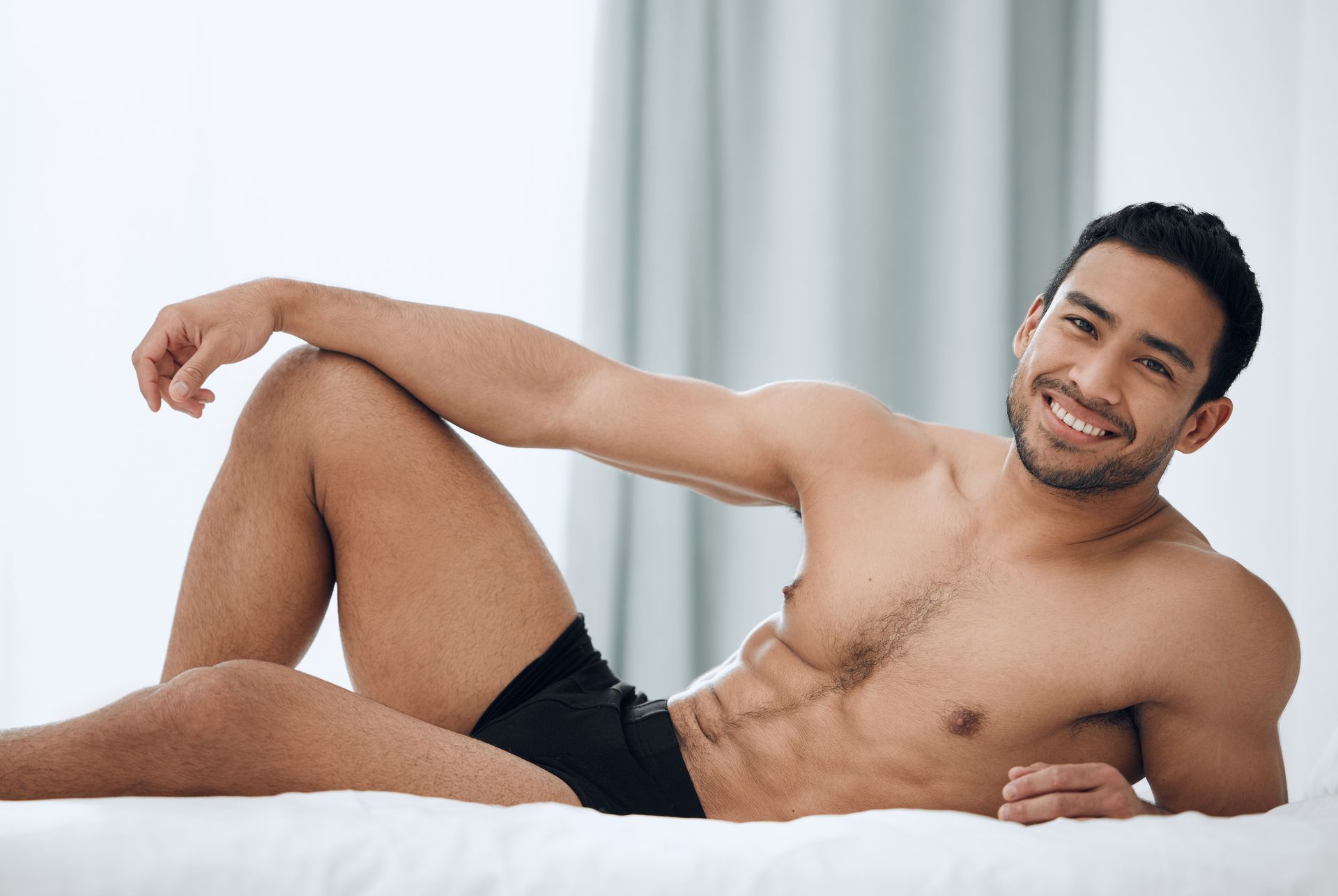 A man in underwear lying on bed with his hand on his knee