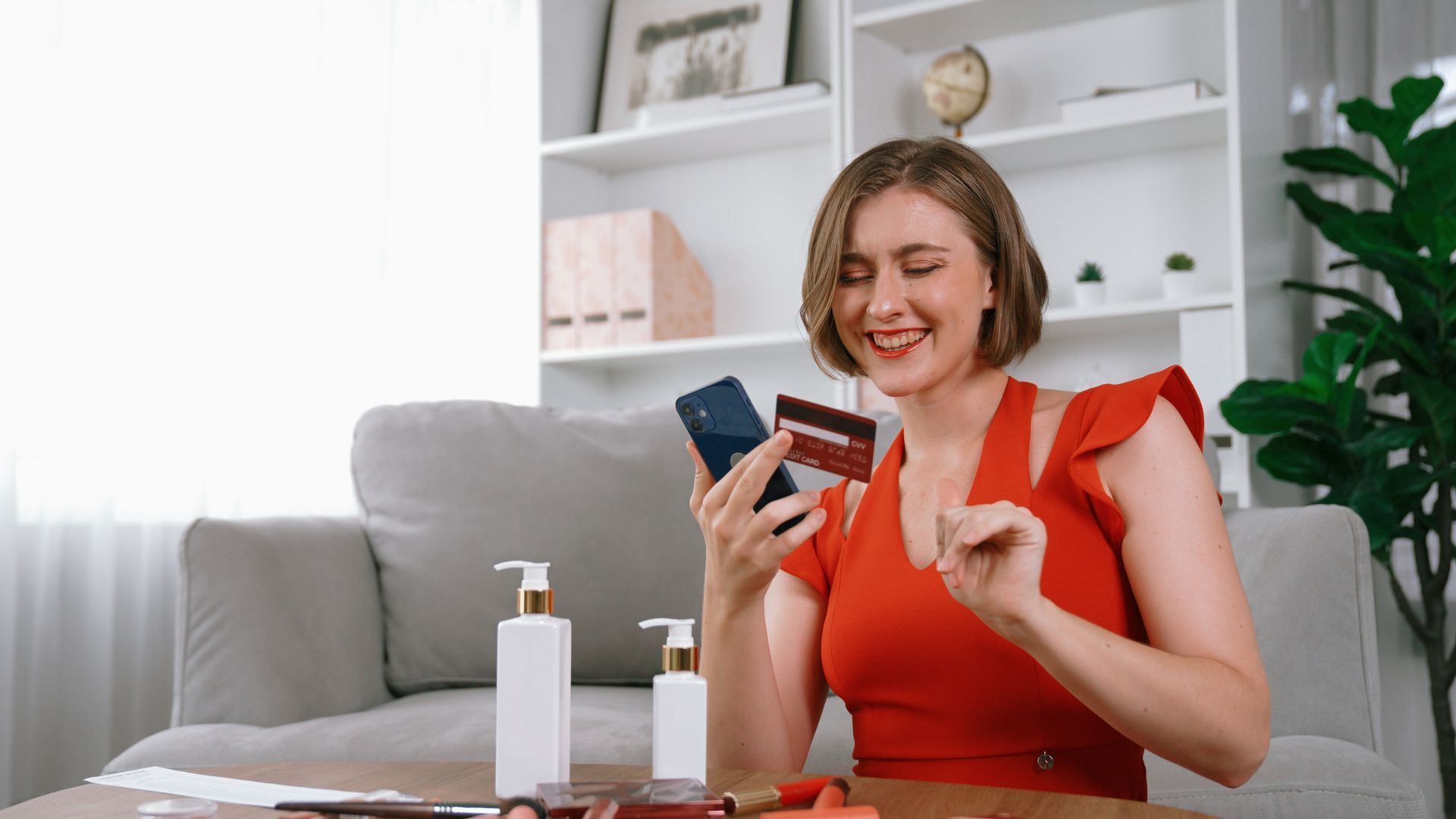 A woman is sitting at a table holding a credit card and a cell phone.
