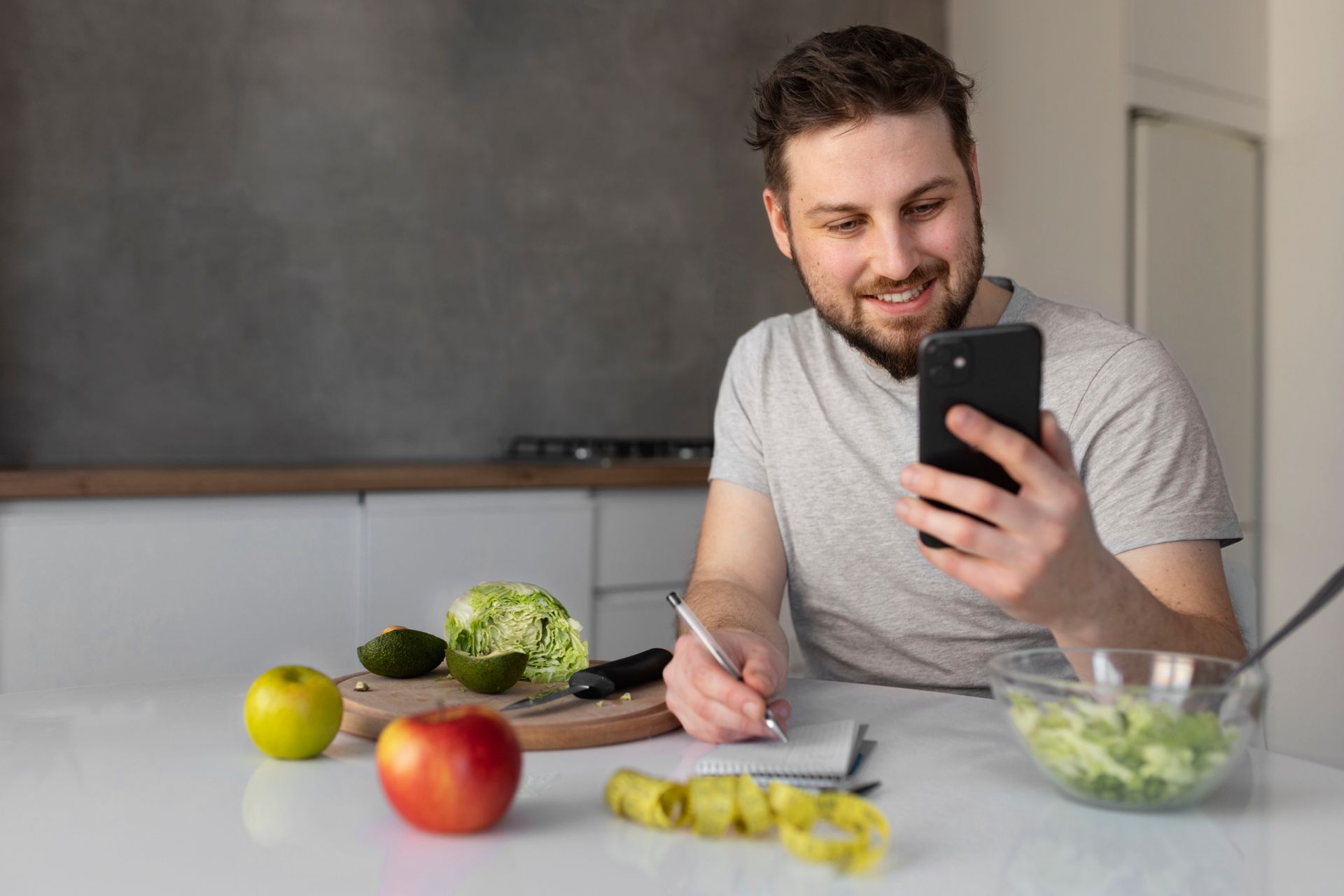 A man is sitting at a table in a kitchen looking at his cell phone.