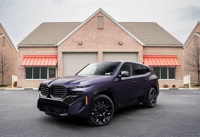 Purple BMW XM SUV parked in front of a brick building with red awnings.