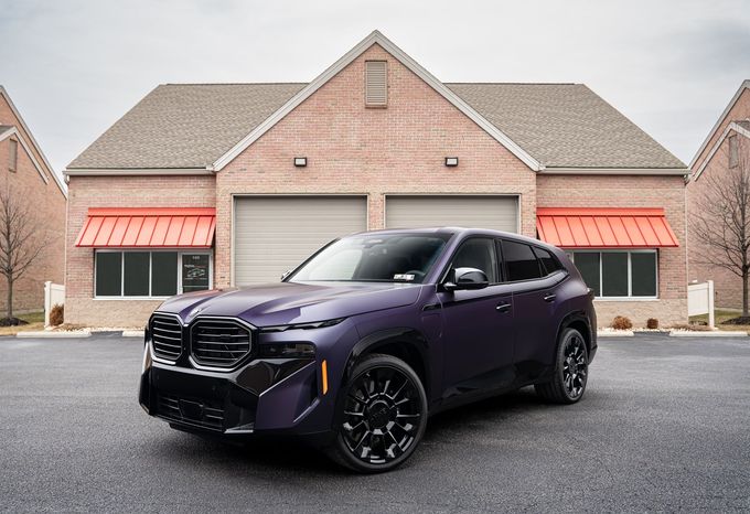Purple BMW XM SUV parked in front of a brick building with red awnings.