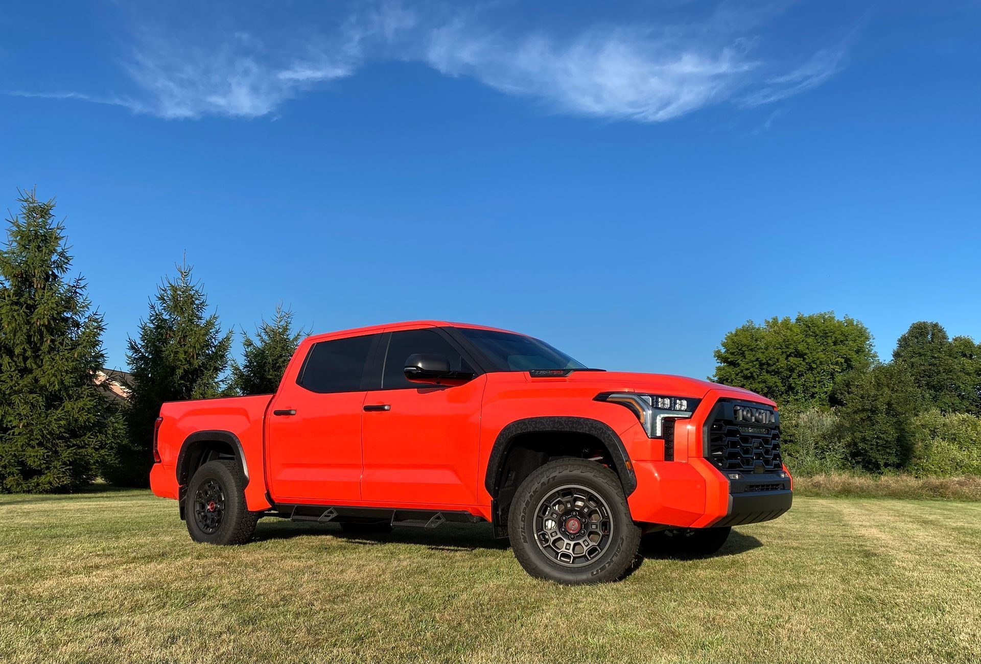 Bright orange Toyota Tundra truck parked on green grass under a blue sky.