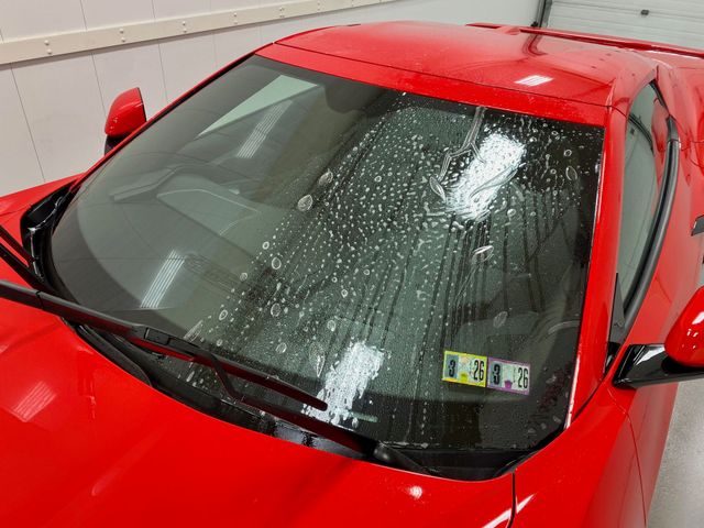 Red sports car with soapy water on the windshield, parked indoors.