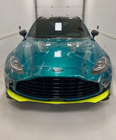 Teal Aston Martin DBX SUV with neon yellow accents parked indoors.