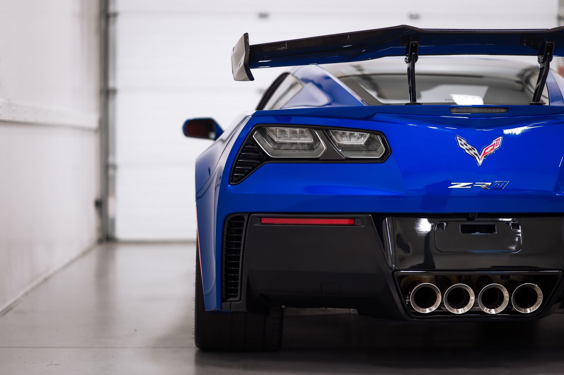 Blue Chevrolet Corvette with large spoiler, parked in a garage.
