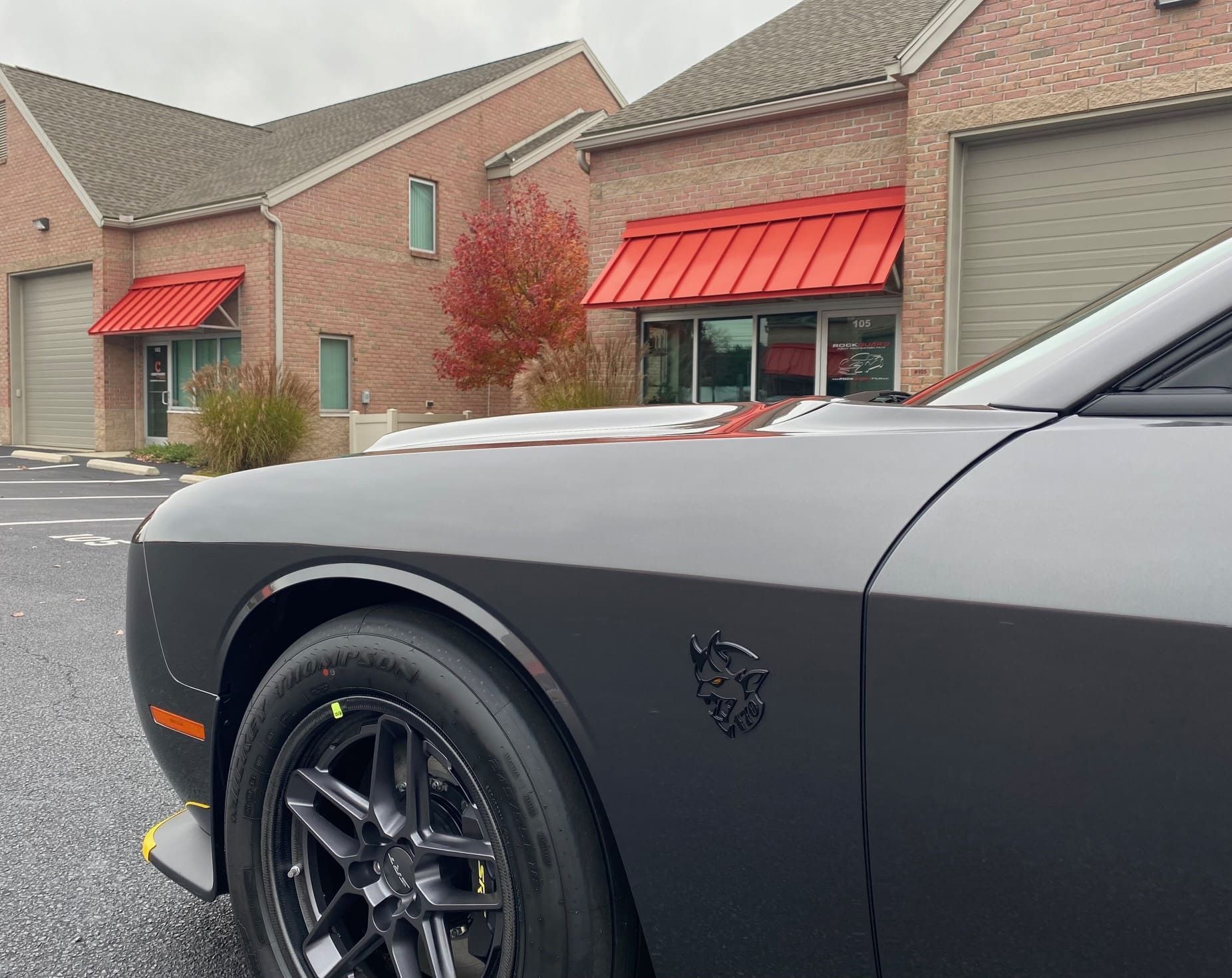 Dark gray Dodge Challenger with black wheels parked near a brick building with red awnings.