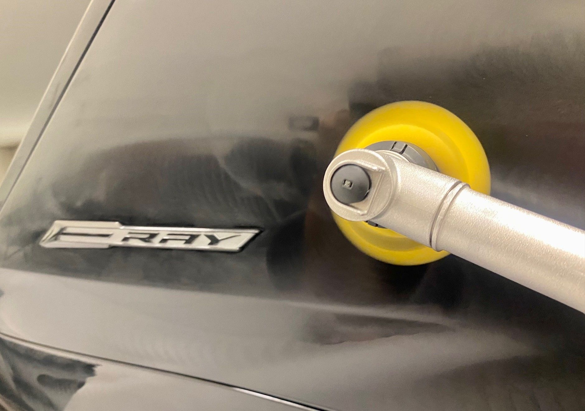 A car's black surface being worked on with a yellow suction tool. 