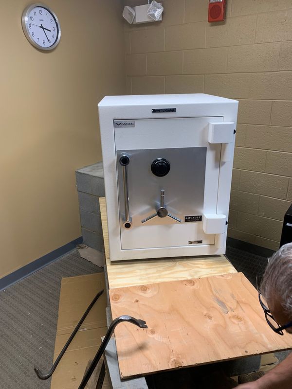 A man is working on a safe in a room with a clock on the wall