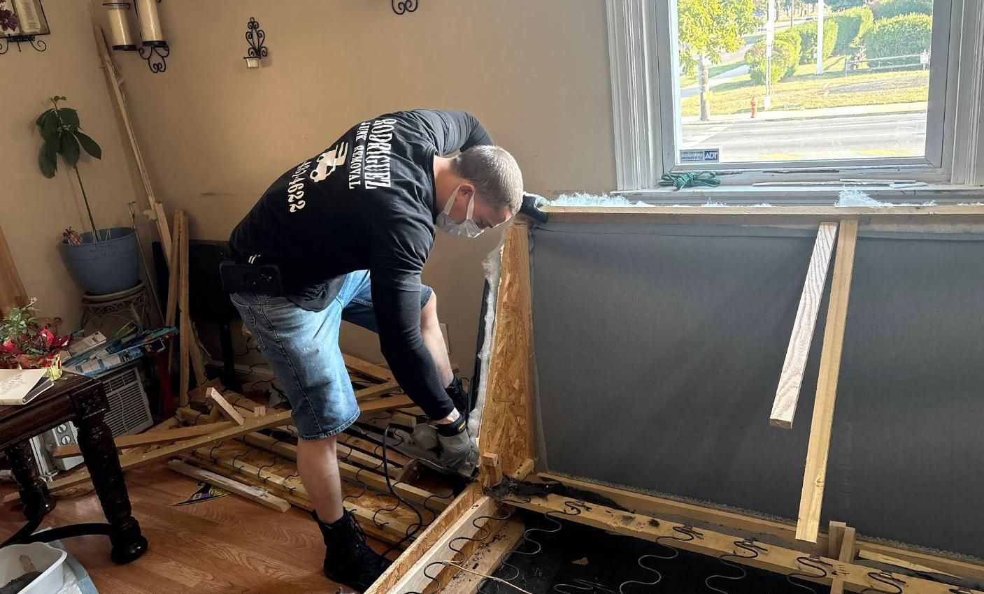 Person in black shirt and shorts working on wall, near window and furniture.
