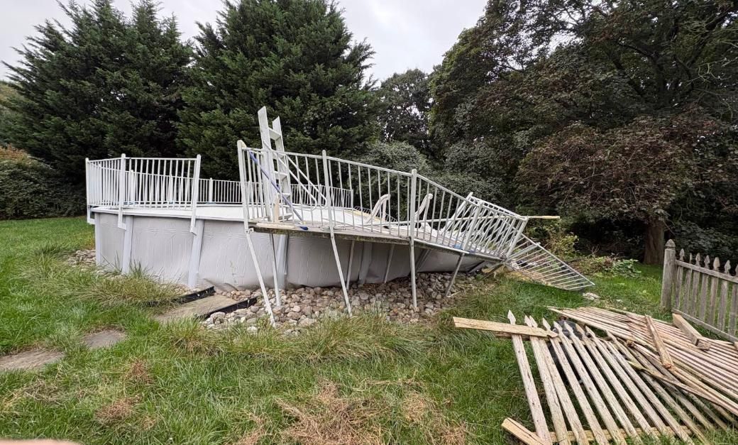 Damaged above-ground pool with collapsed deck in a grassy backyard.