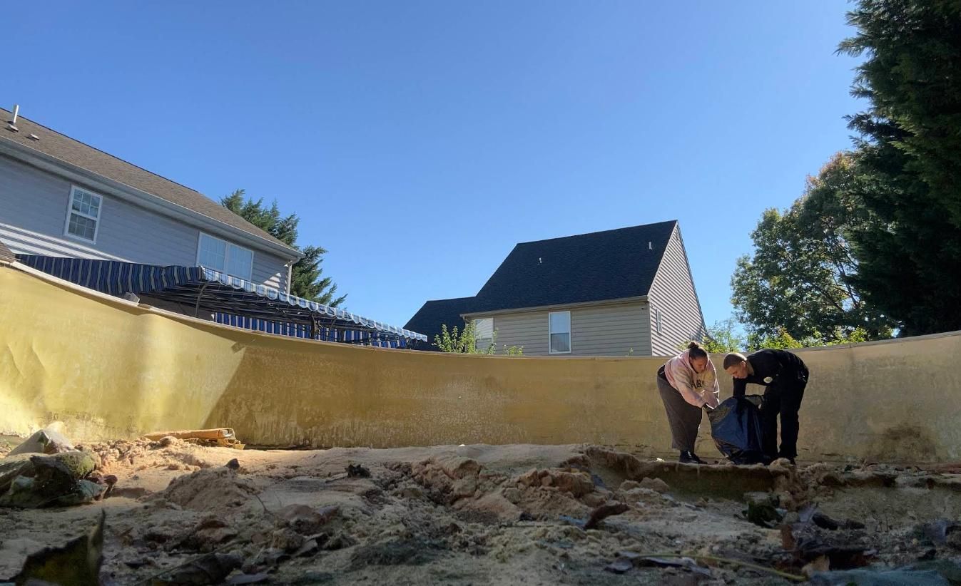 Three people working in a drained pool.  Light brown walls and dirt on the bottom. 