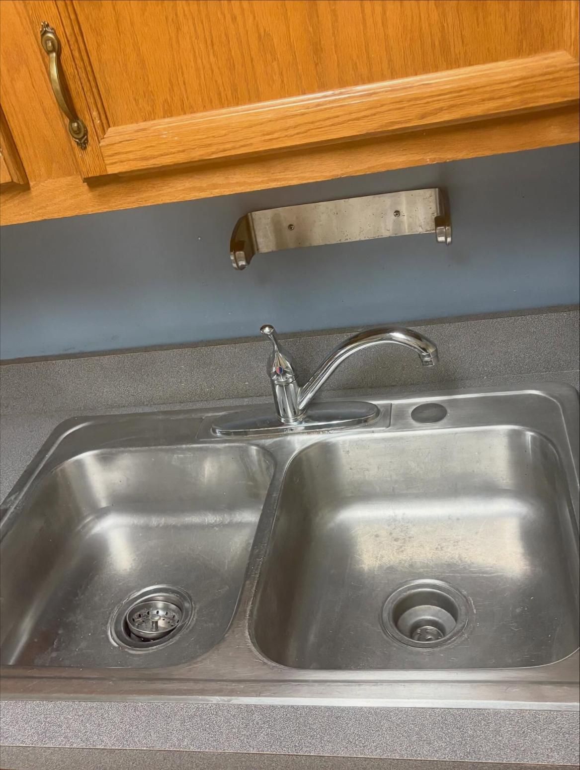 Stainless steel double sink with faucet, under wooden cabinets.