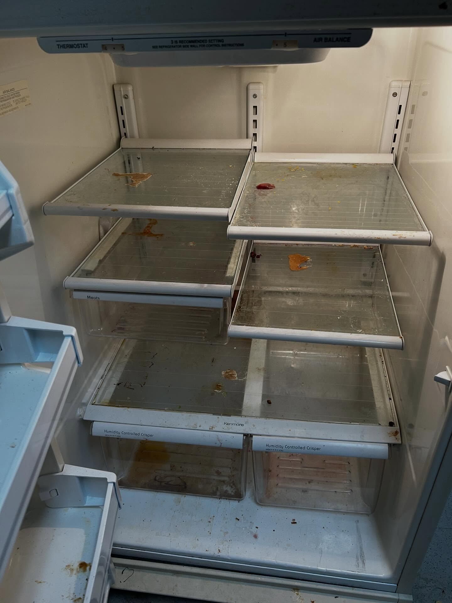 Empty and dirty refrigerator interior with glass shelves and drawers.
