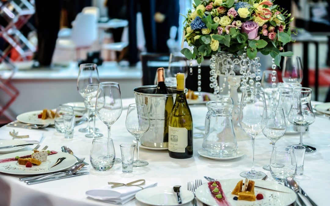 photo of a table at a classy event with wine glasses, wine bottles, plates and silverware.