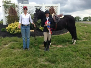Two women standing next to a black horse holding a ribbon.