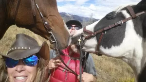 A woman in a cowboy hat is taking a selfie with two horses.