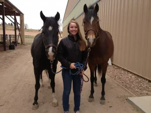 A woman standing between two horses holding a leash