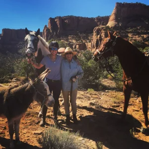 Two women standing next to two horses and a donkey