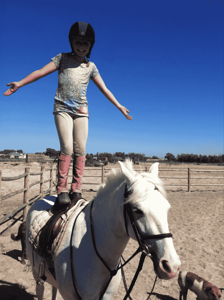A young girl is riding a white horse with her arms outstretched