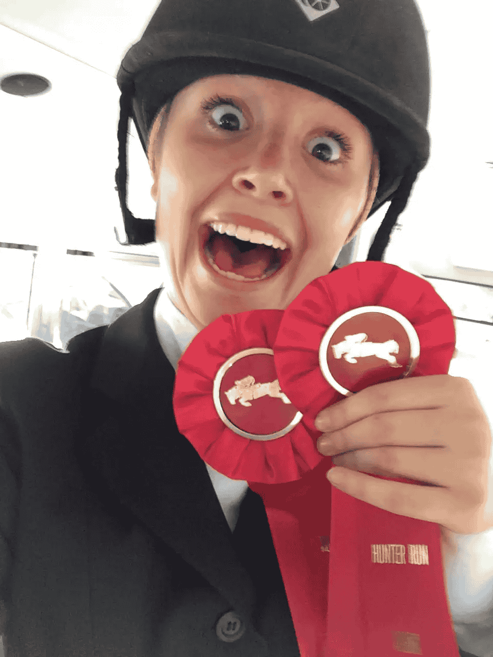 A woman wearing a helmet is holding a red ribbon with a horse on it