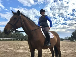 A woman is riding a brown horse in a dirt field.