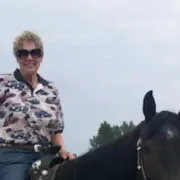 A woman is riding on the back of a black horse.