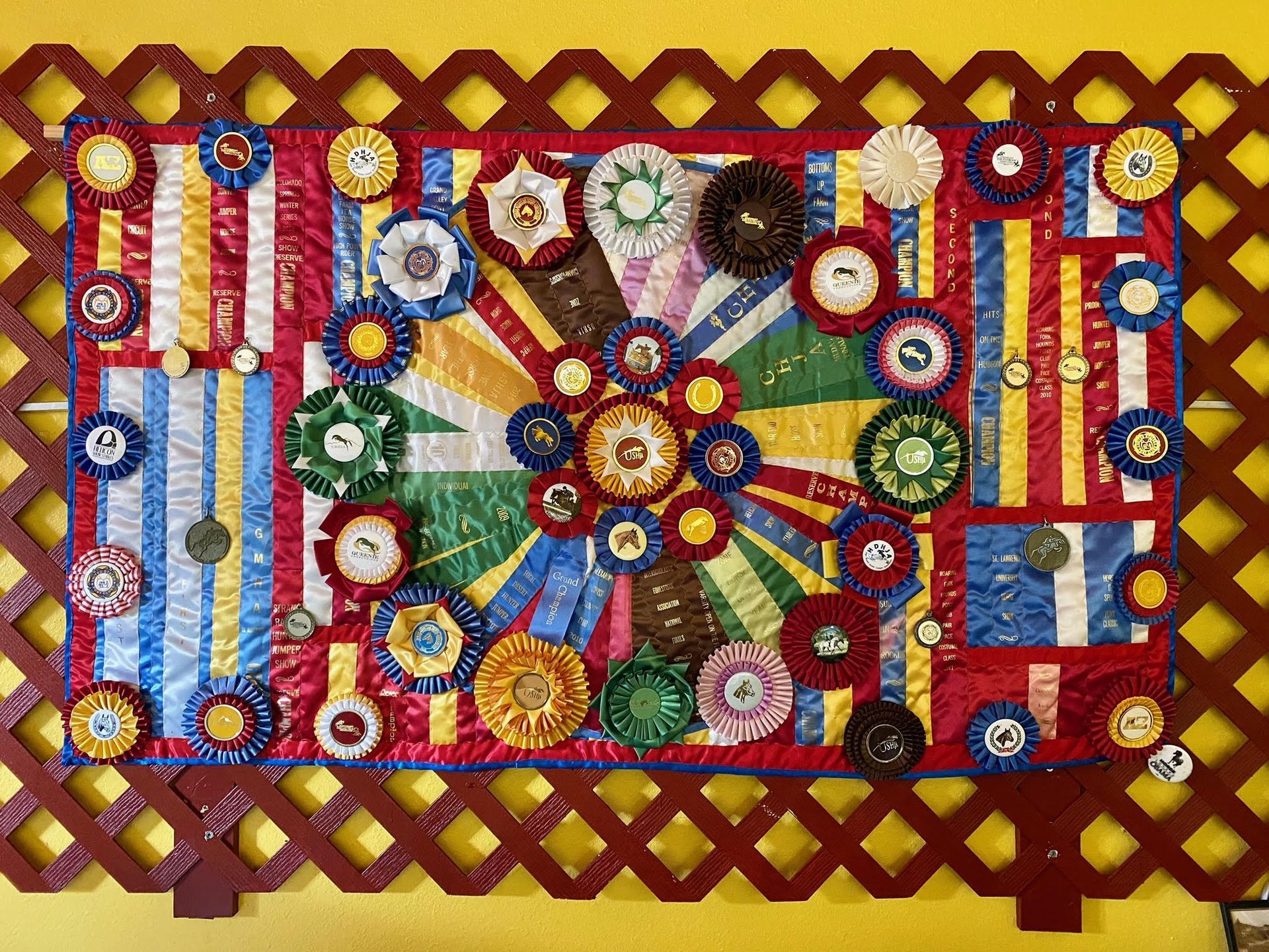 A quilt with ribbons on it is hanging on a wooden fence.