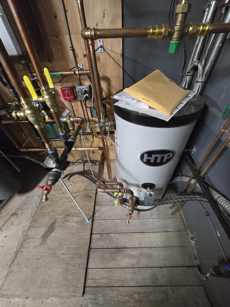 Copper pipes and water heater in a utility room with wooden floor.