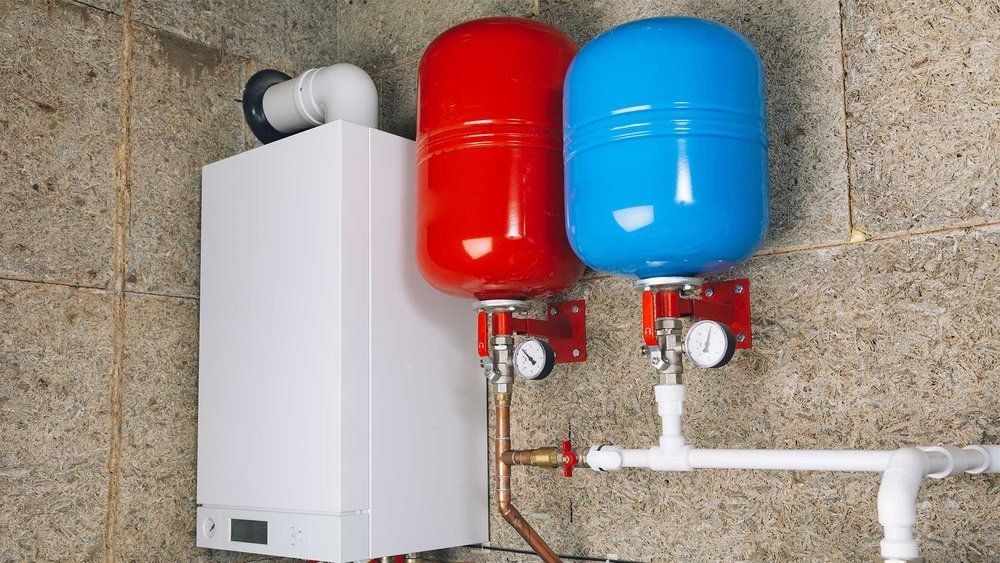 White furnace next to red and blue expansion tanks on a concrete wall. Plumbing visible.