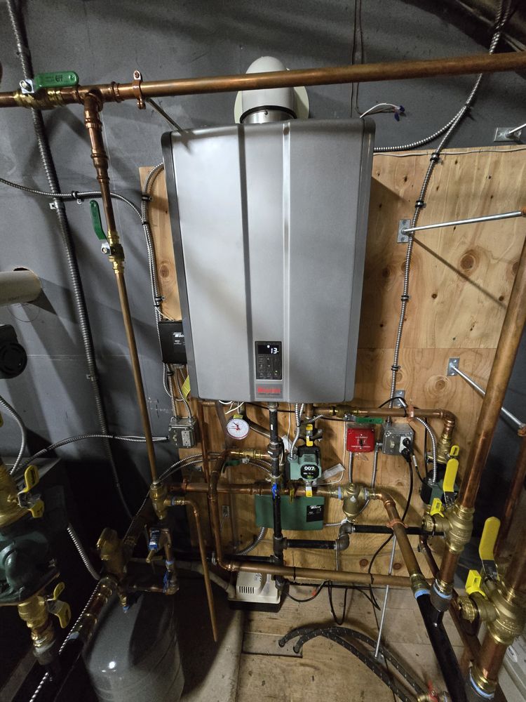 A wall-mounted, silver tankless water heater with copper piping in a utility room.