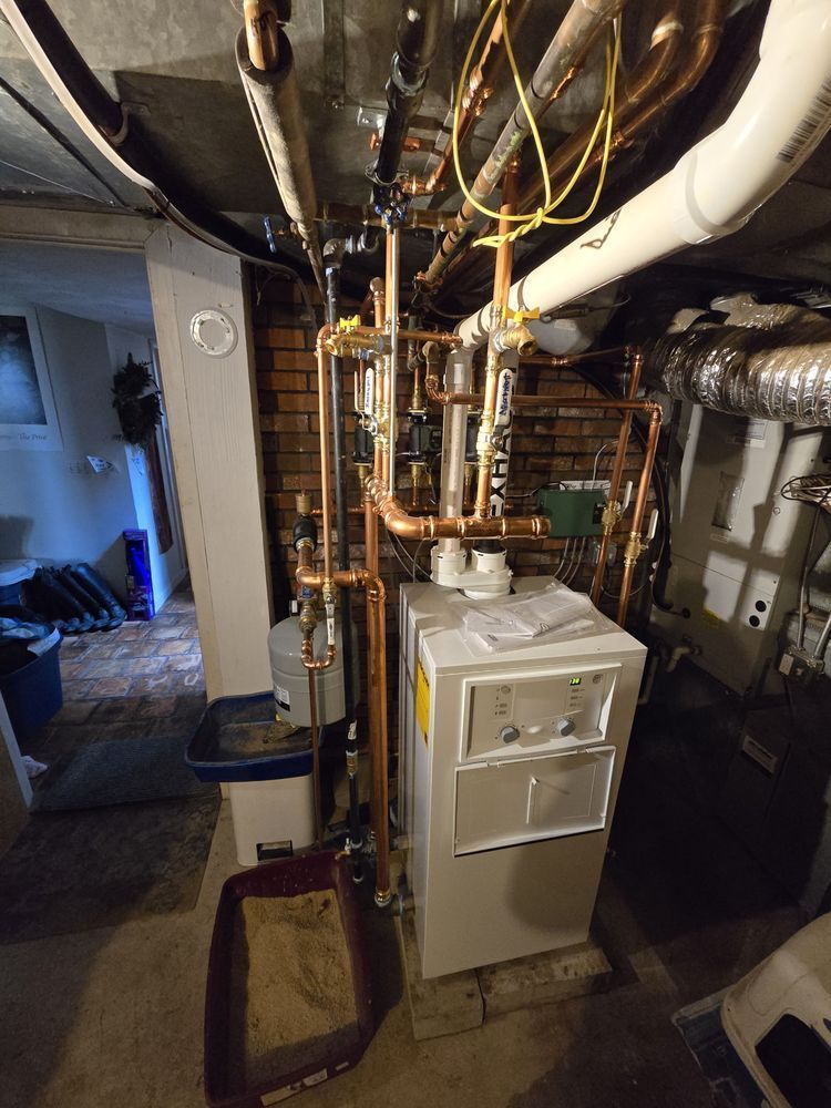 Copper pipes and a white water heater installed in a basement against a brick wall.