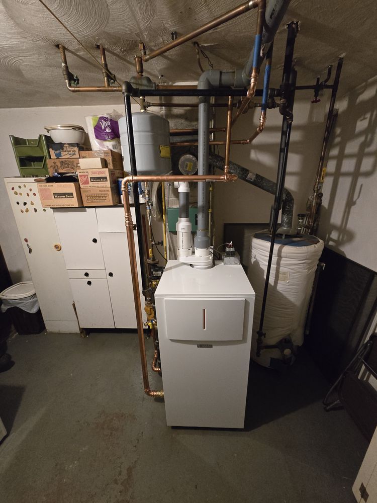 A basement with a white boiler, copper pipes, and a water heater; storage cabinets are on the left.